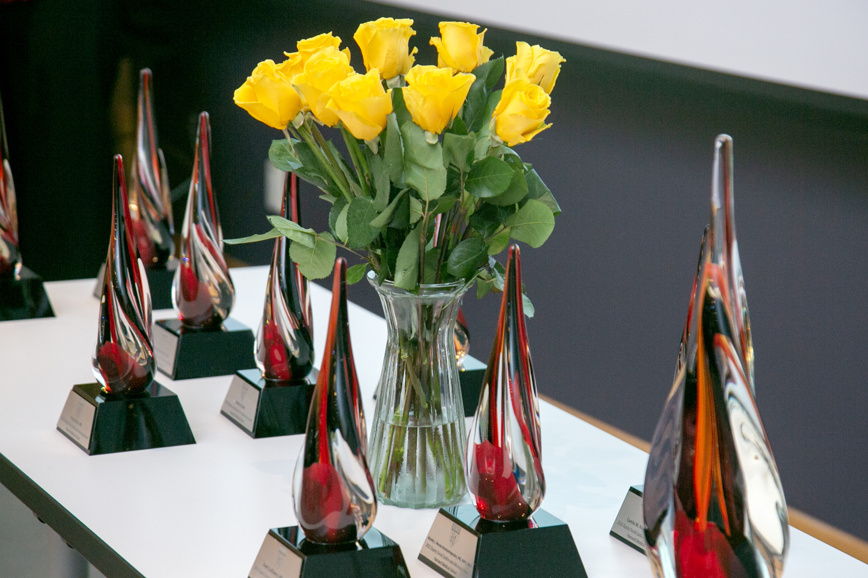 The ESJA Awards, shaped like red glass droplets, sit on a table alongside a vase of yellow roses. 