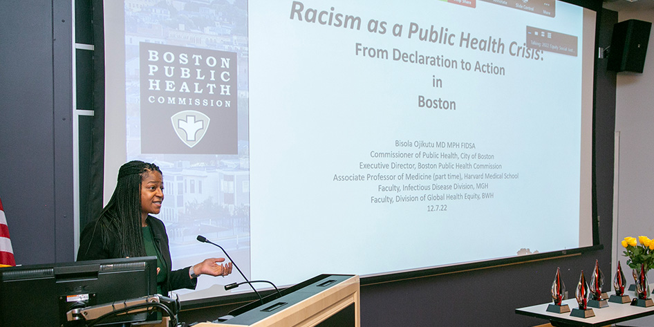 Bisola Ojikutu speaks at a podium by her presentation,'Racism as a Public Health Crisis: Declaration to Action in Boston.'