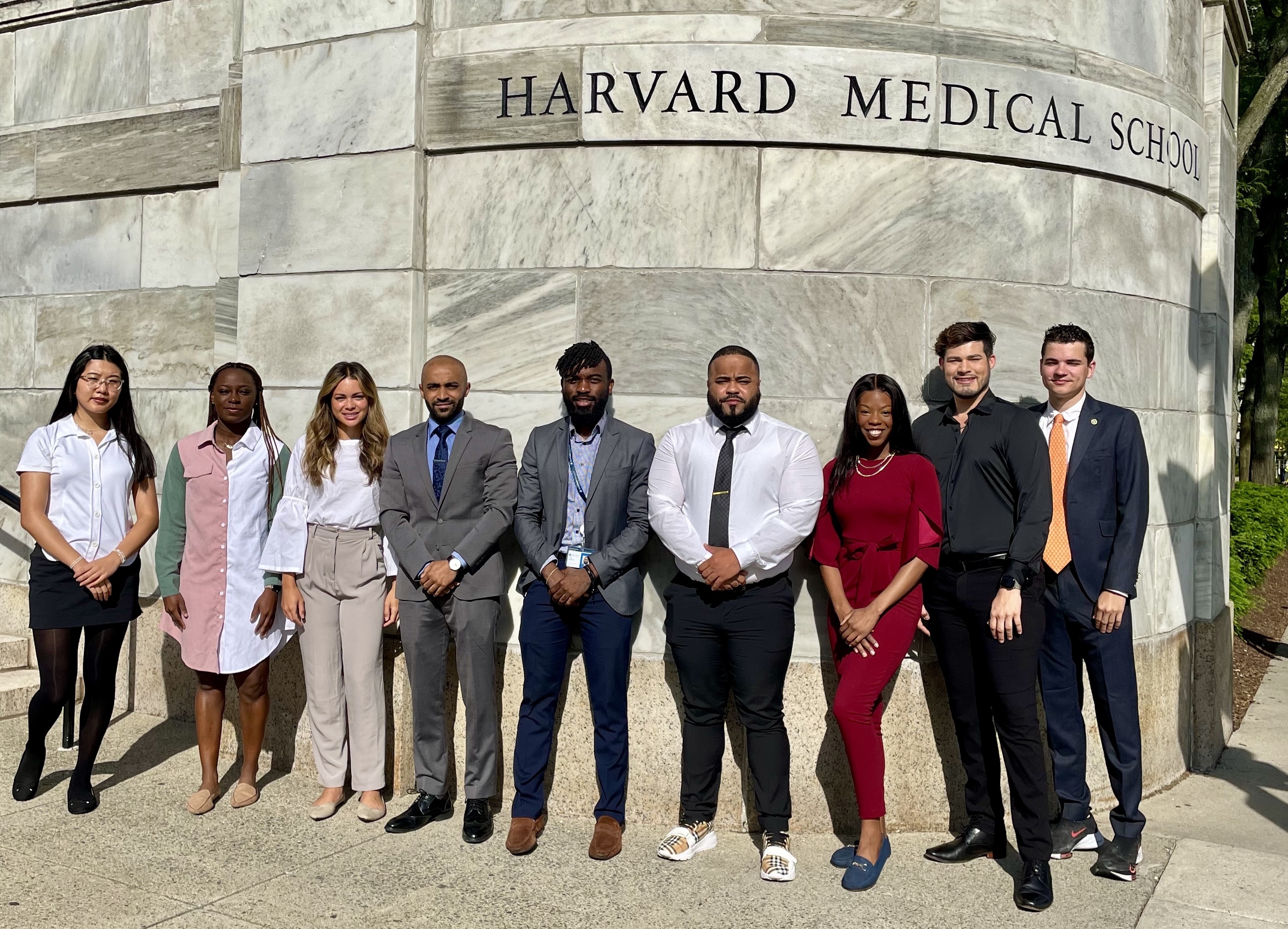 All nine 2023 VRIP interns stand in front of the large marble wall by Harvard Medical School. 