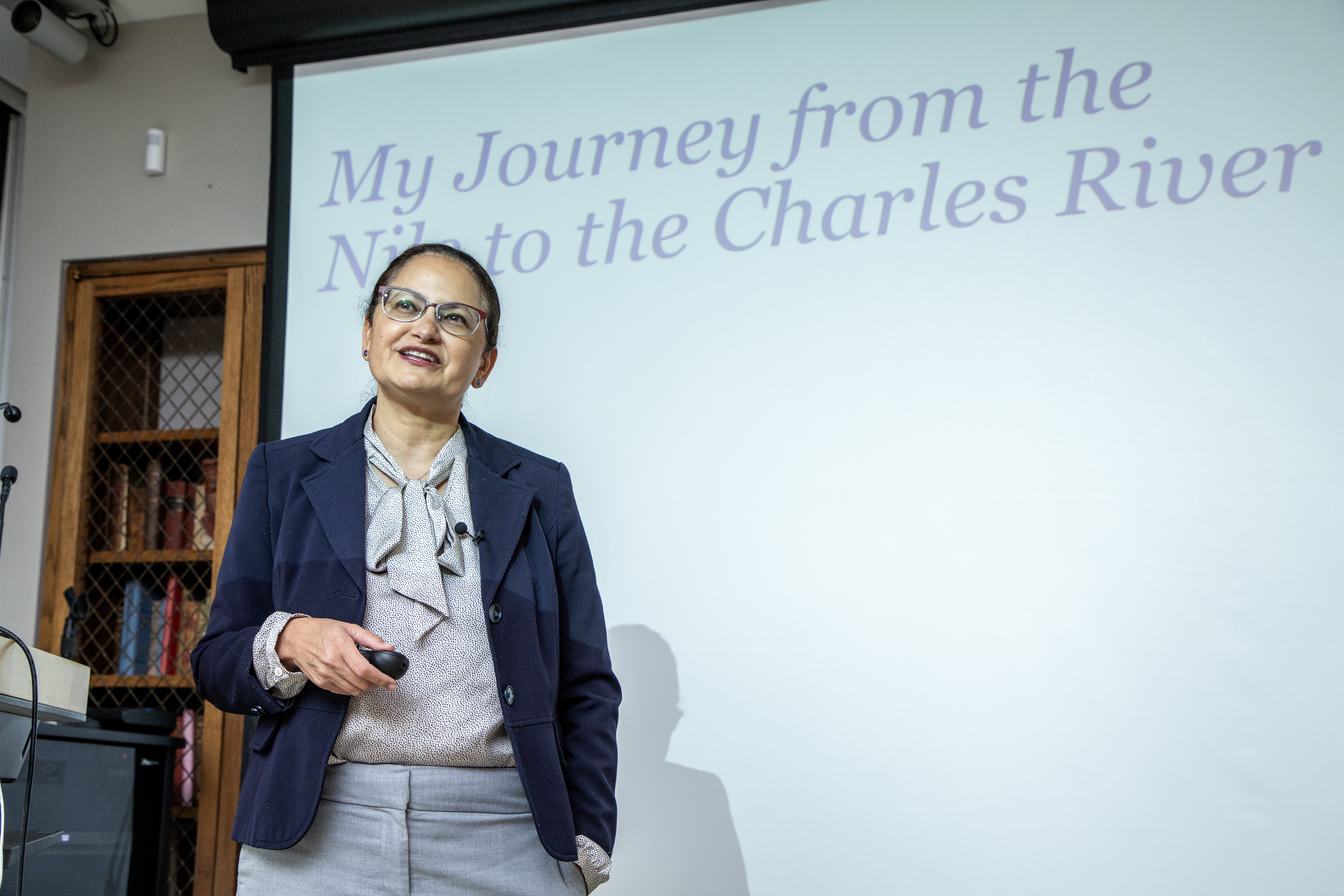 Nawal Nour stands in front of a projector screen with her presentation title, 'My Journey from the Nile to the Charles River.'