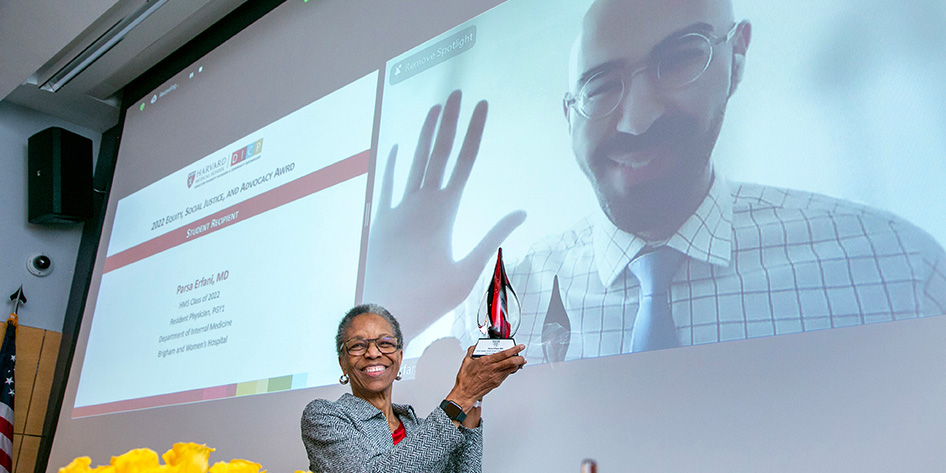 Joan Reede holds up an ESJA award while recipient Parsa Erfani waves from a virtual Zoom room in the background.